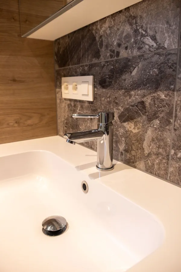 Witte lavabo met chromen kraan tegen een wand in bruine natuursteenlook, realisatie van ID Interieur