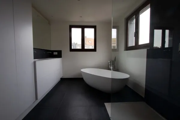 Ruime badkamer met vrijstaand bad, zwarte vloer en maatkasten, realisatie van ID Interieur