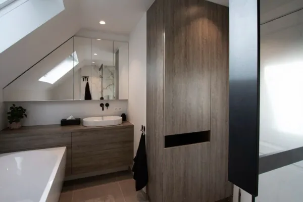 Zolderbadkamer met houten badmeubel en hoge kast op maat, realisatie van ID Interieur