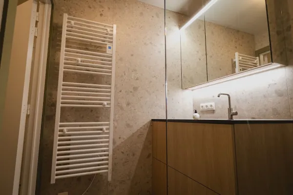Badkamer met witte handdoekradiator, terrazzo en houten badmeubel, realisatie van ID Interieur