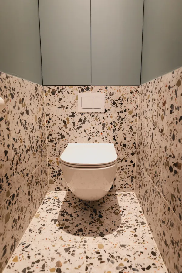 Toilet in terrazzo met groene kasten erboven, realisatie van ID Interieur