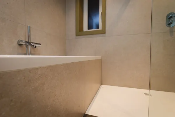 Bad en douche in een badkamer met grote zandkleurige tegels, realisatie van ID Interieur
