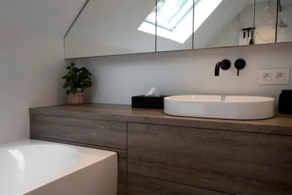 Zolderbadkamer met waskom op houten badmeubel en zwarte kraan, realisatie van ID Interieur