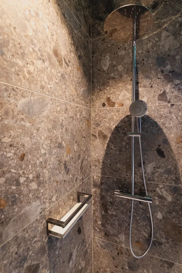Douche met wanden in bruine natuursteenlook en douchestang, realisatie van ID Interieur