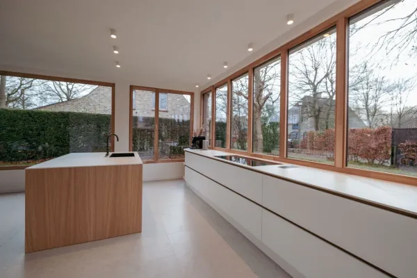Lange witte keuken met eiken eiland langs een raampartij, realisatie van ID Interieur