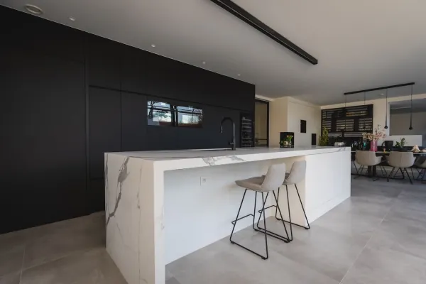 Keuken met marmerlook kookeiland, barkrukken en zwarte kastenwand, realisatie van ID Interieur