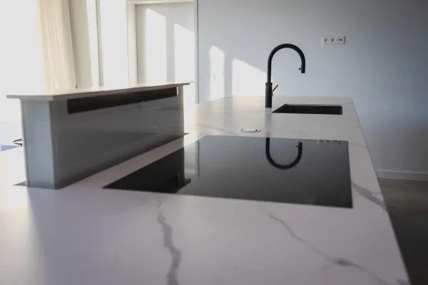Kookeiland in marmerlook met kookplaat en zwarte kraan, realisatie van ID Interieur