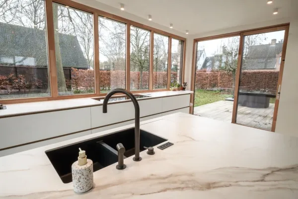 Werkblad in marmerlook met zwarte spoelbak en zicht op de tuin, realisatie van ID Interieur