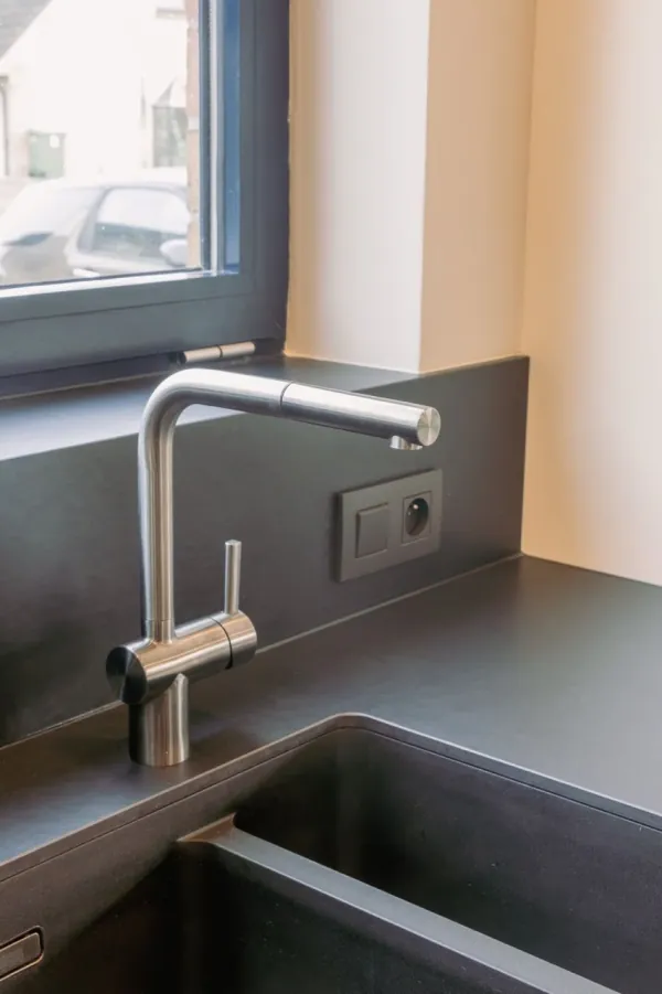 Inox kraan boven een zwarte spoelbak in een donker werkblad, realisatie van ID Interieur