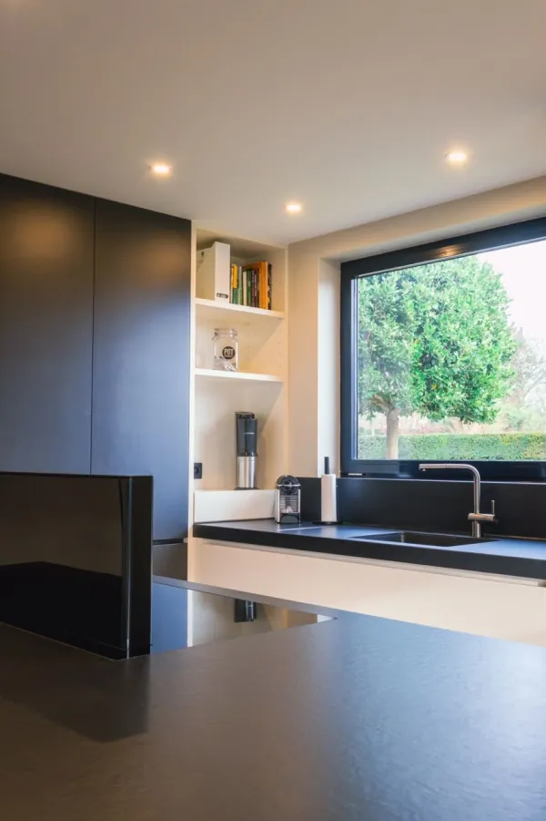 Donkere keuken met zwart werkblad en raam naar de tuin, realisatie van ID Interieur