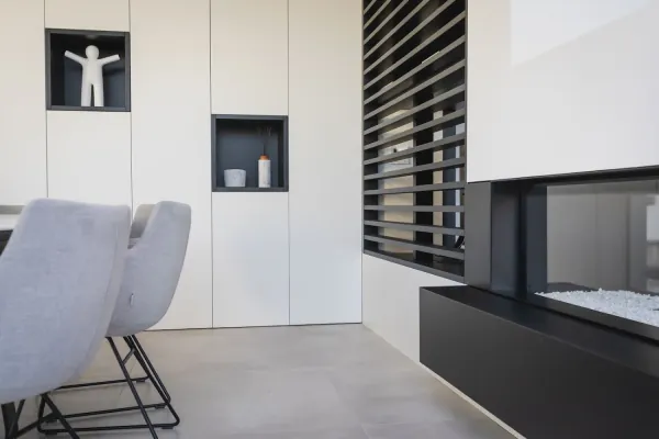 Witte kastenwand met nissen en lamellen naast een gashaard, realisatie van ID Interieur