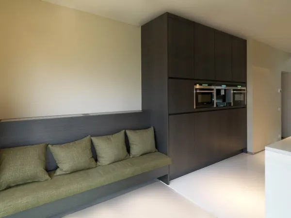 Donkere kastenwand met inbouwtoestellen en zitbank, realisatie van ID Interieur